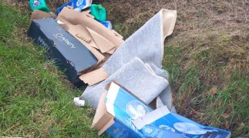 cardboard boxes and carpet fly tipped on the side of a verge